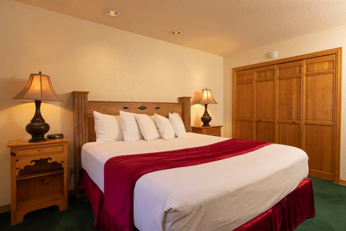 A peaceful bedroom with red-accented bedding, soft lighting from bedside lamps, and a wooden closet. The layout creates an inviting, restful space ideal for relaxation or quiet moments after a day of adventure.