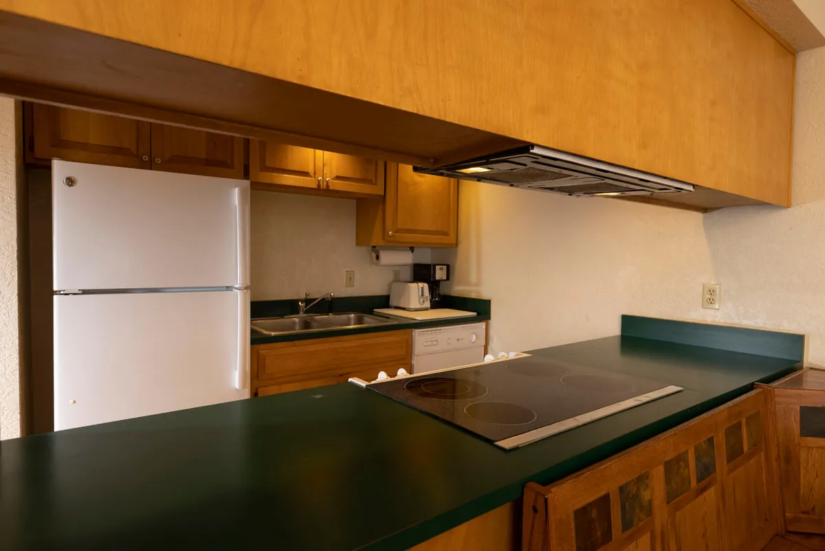A view of the kitchen space, focusing on the kitchen countertop, stove, refrigerator, and sink. The scene is lively and functional, with the layout encouraging both cooking and social interaction. The modern finishes and open sightlines invite participation and make the space feel welcoming.