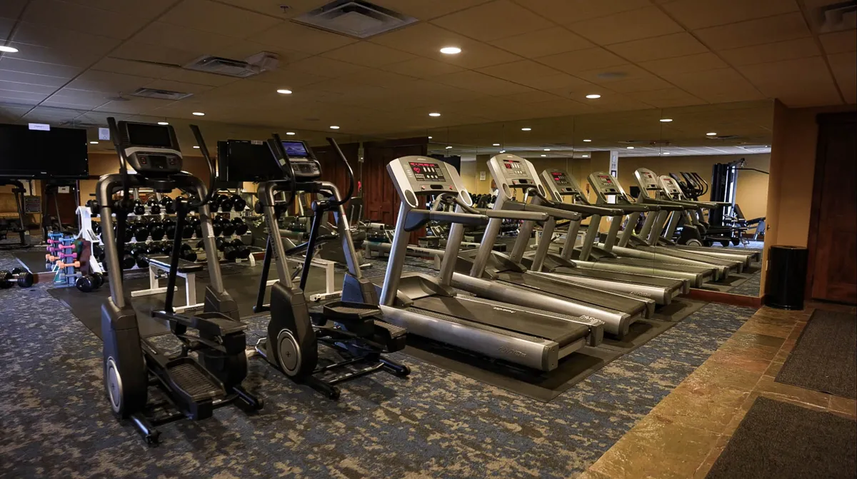 A well-equipped fitness center featuring elliptical machines, treadmills, and a rack of dumbbells set against a mirrored wall. The space is bright and inviting, designed to inspire motivation and accommodate both individual workouts and group fitness classes.