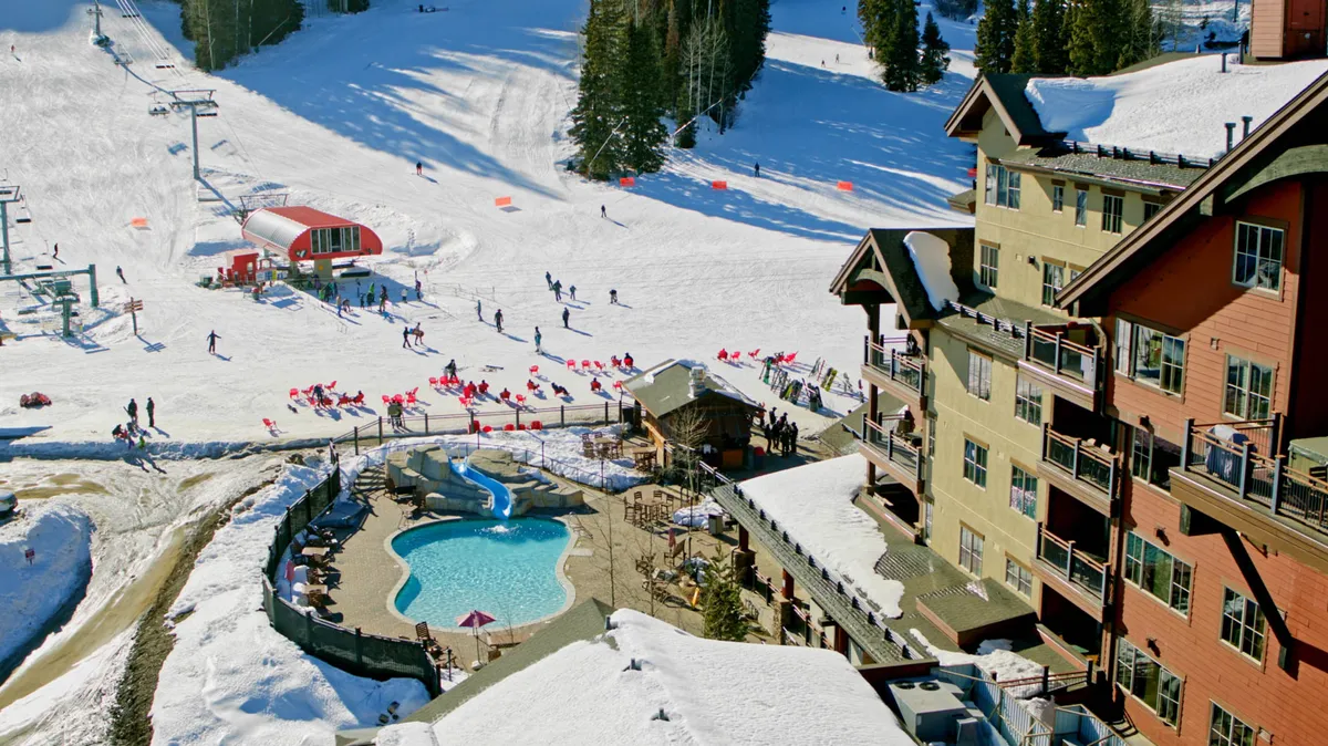 An exterior scene showcasing lodge architecture with ski lifts, skiers on the slopes, and an outdoor pool. The setting is lively and energetic, capturing the mountain resort lifestyle and easy access to skiing and après-ski amenities.